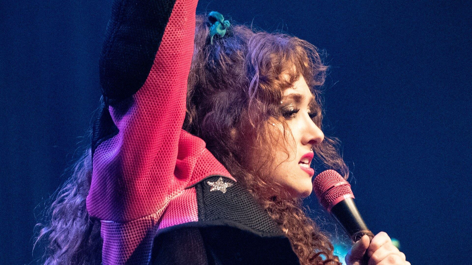 Chappell Roan performing onstage with a microphone, one arm raised